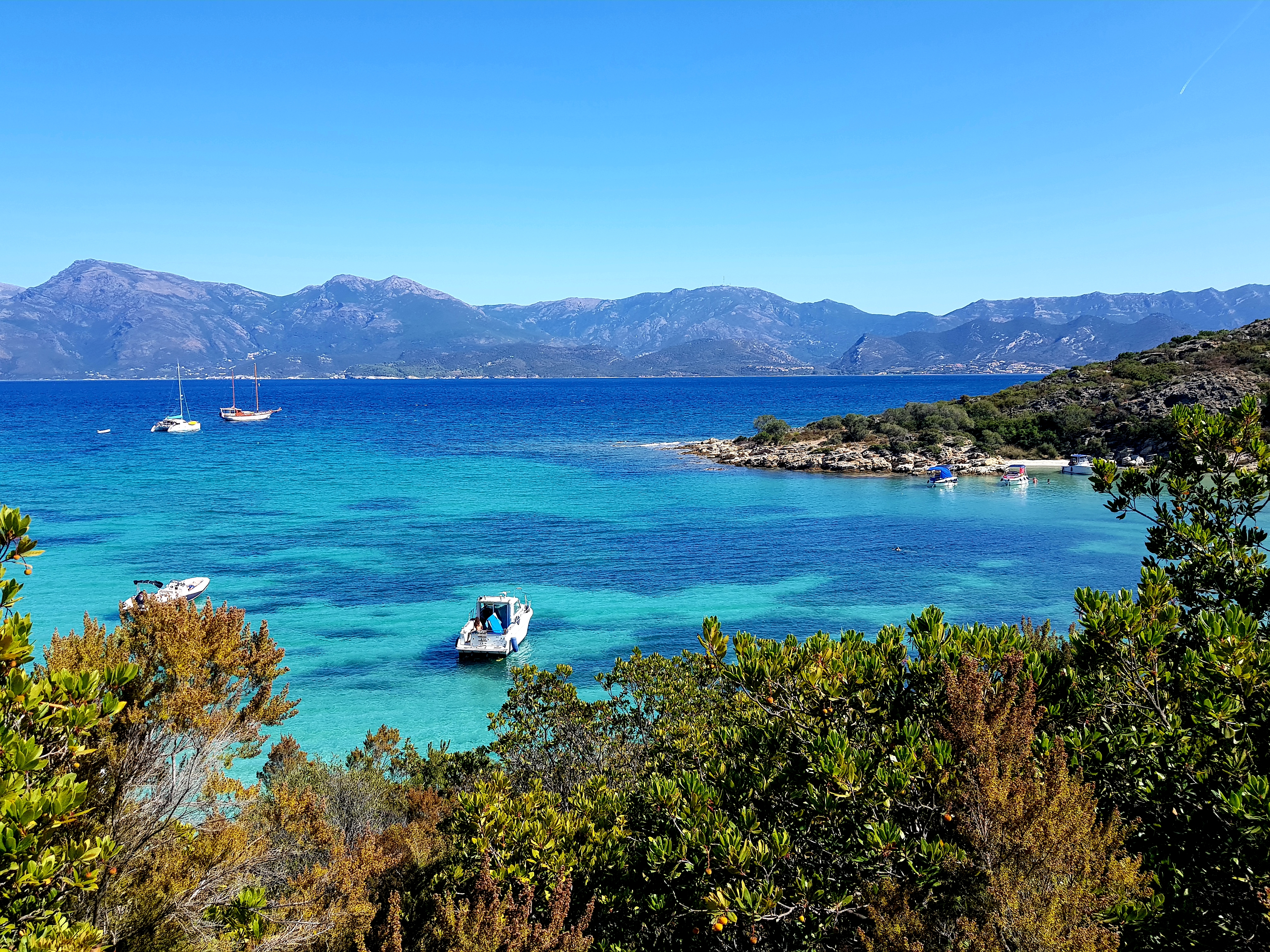 Crique aux eaux turquoise à Saint-Florent avec bateaux ancrés et montagnes corses en arrière-plan.