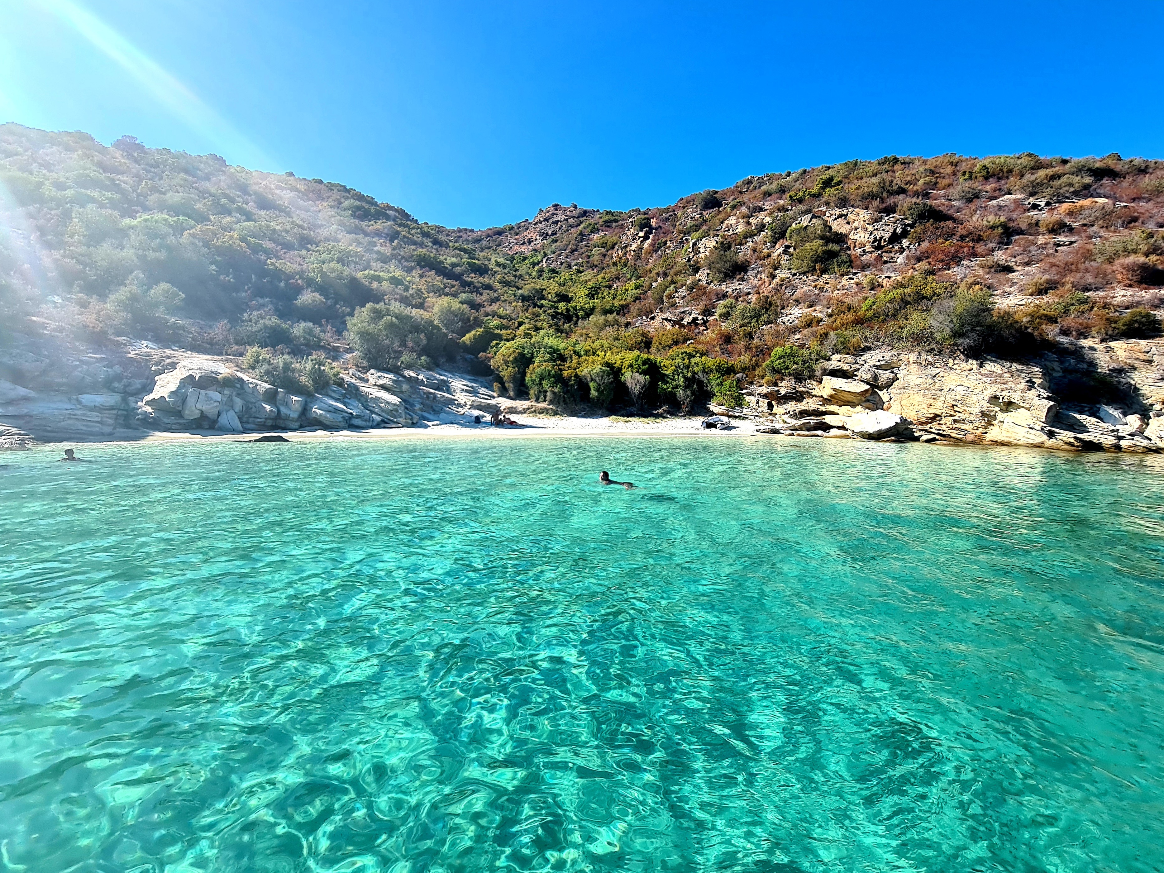Crique isolée aux eaux cristallines avec plage de sable blanc et maquis corse verdoyant.