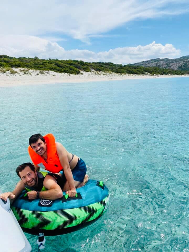 Deux amis sur une bouée tractée profitant des eaux turquoise près d'une plage sauvage corse.
