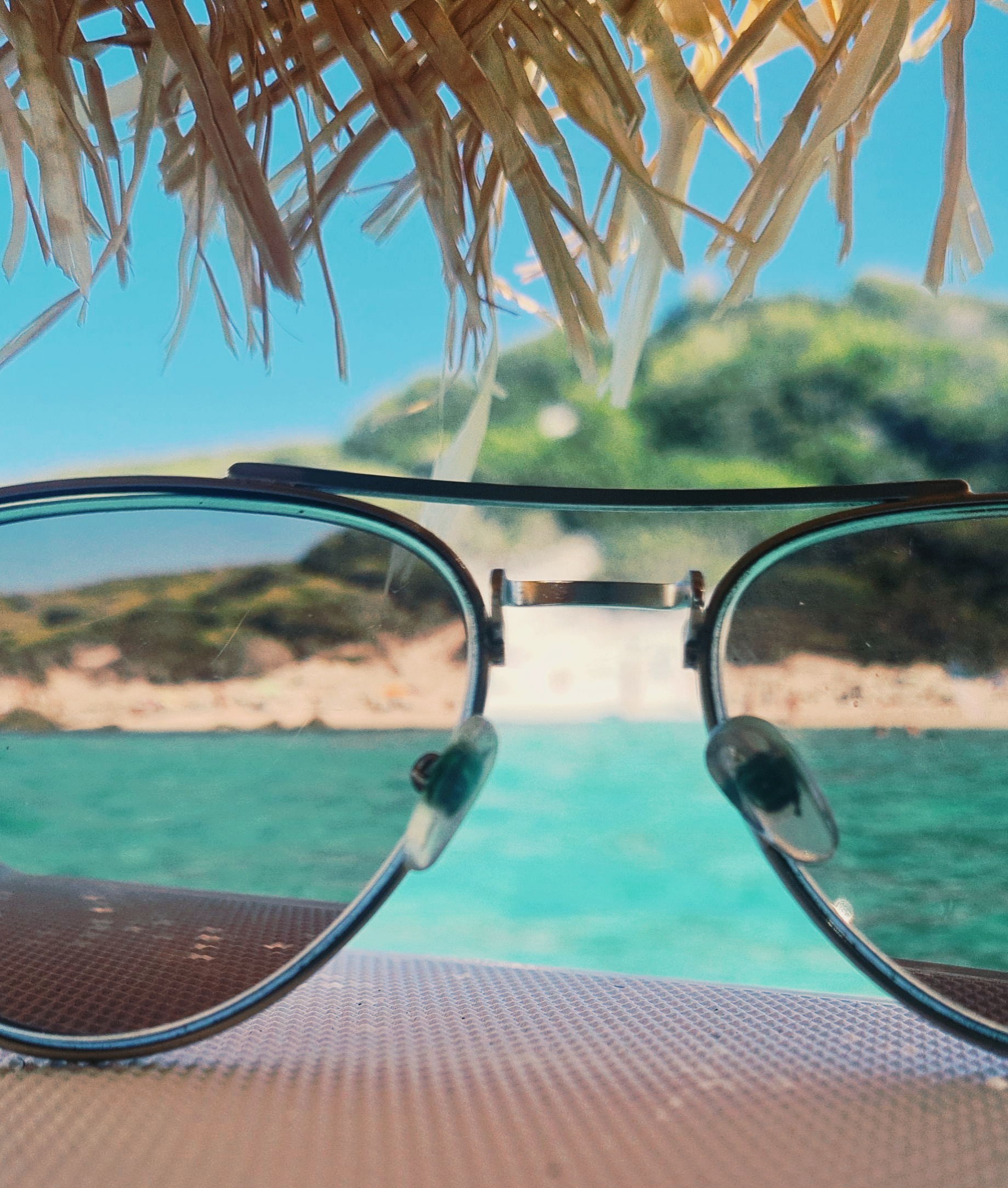 Vue à travers des lunettes de soleil sur une crique paradisiaque et ses eaux émeraude.